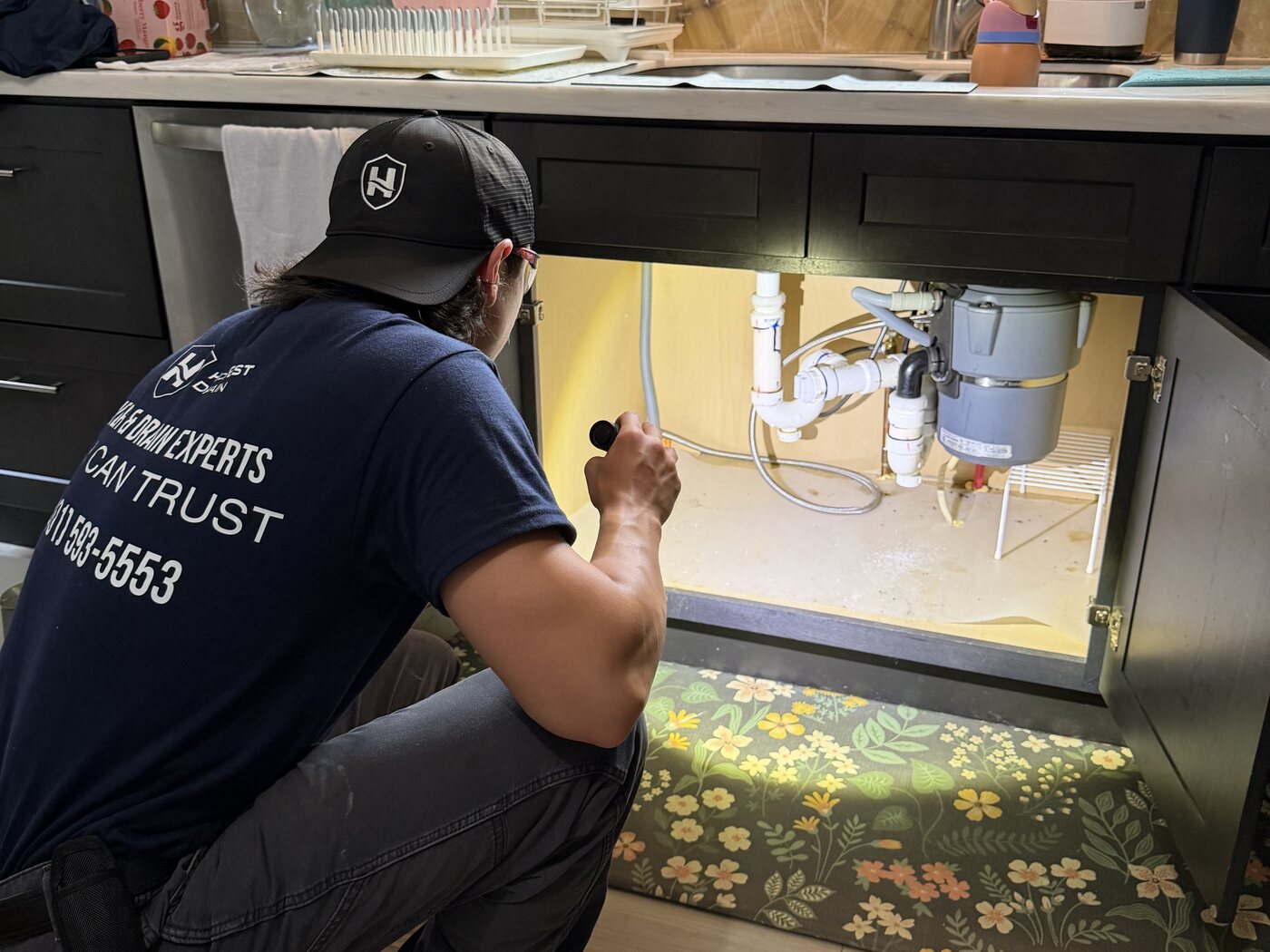 Honest Drain technician inspecting piping under a kitchen sink